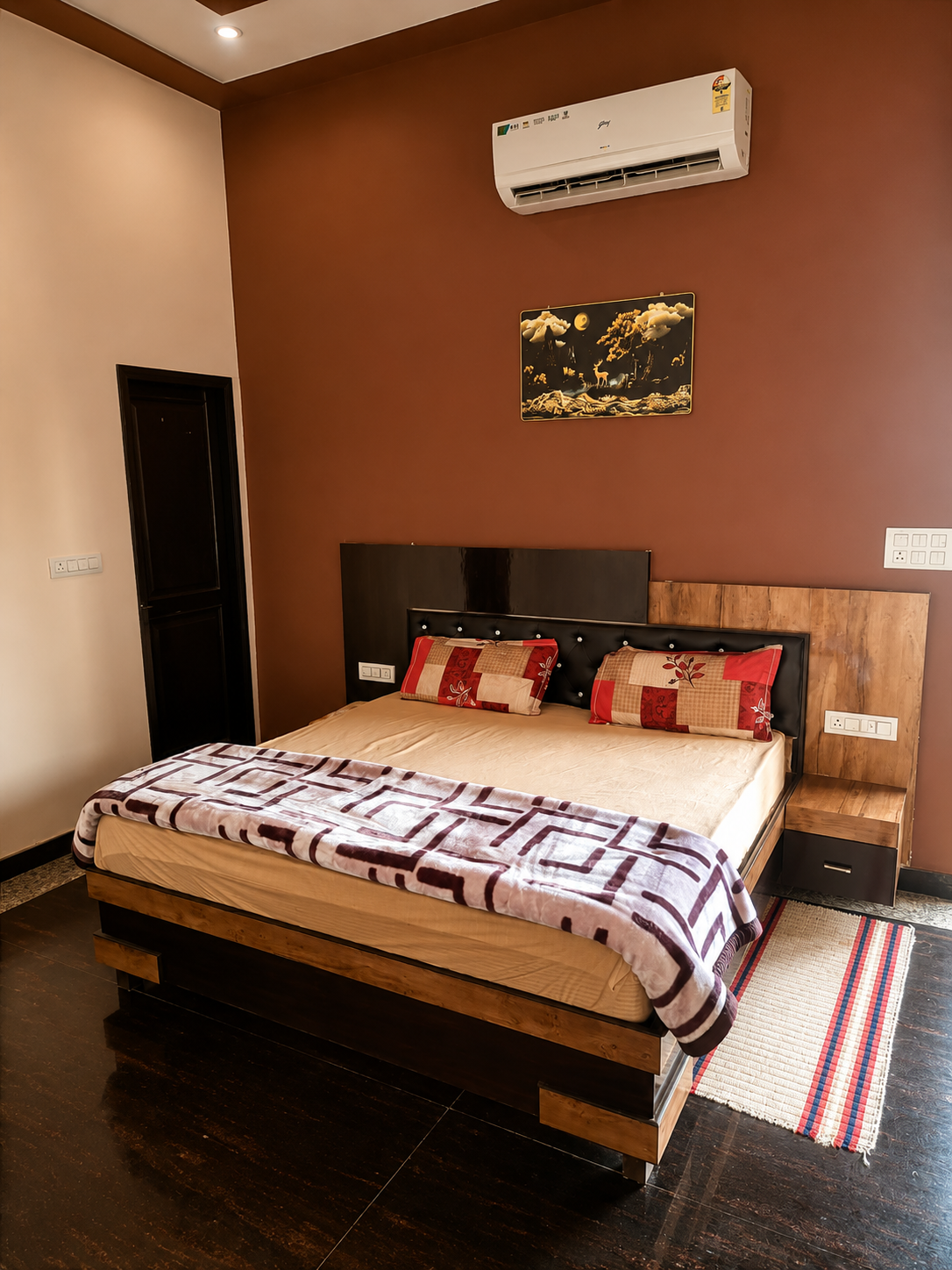 AC bedroom at Mandiya Villa with a king bed, dark wood floor and a warm terracotta feature wall.